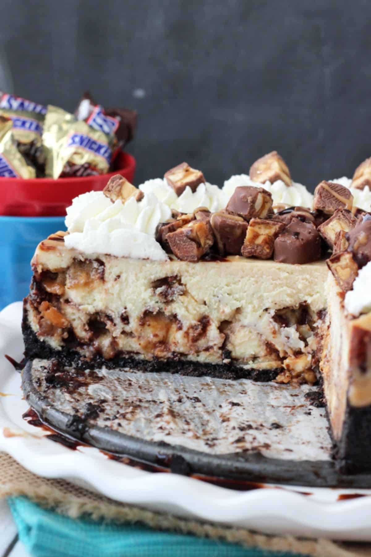 A Snickers cheesecake with a few slices removed to show inside.