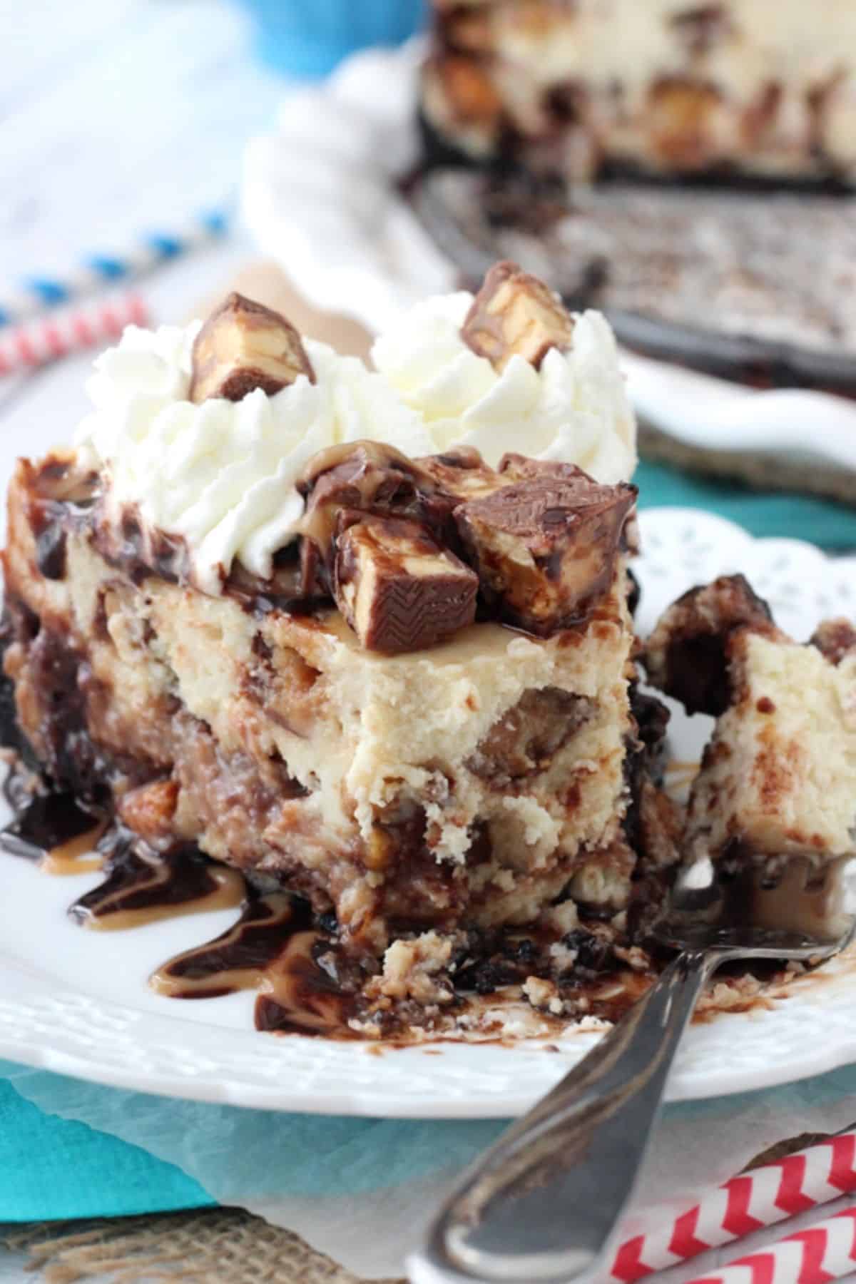 A slice of Snickers cheesecake with a bite removed on a fork.