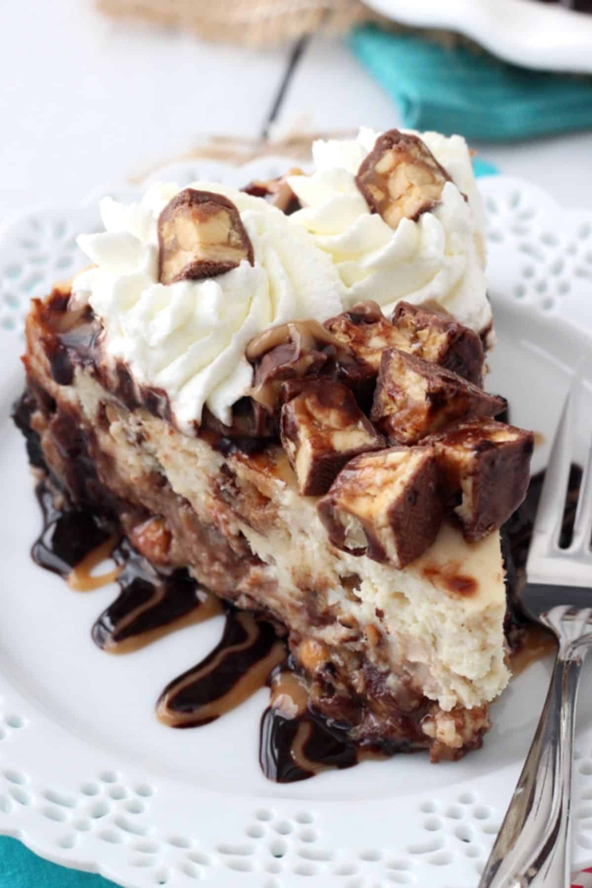A slice of Snickers cheesecake on a small white plate.