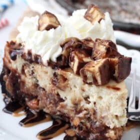 Close up of a slice of Snickers cheesecake on a small white plate.