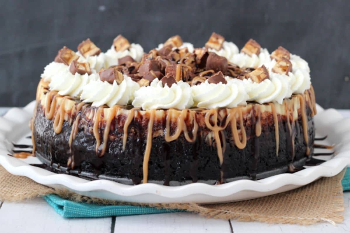 Side view of a Snickers cheesecake on a white cake plate.