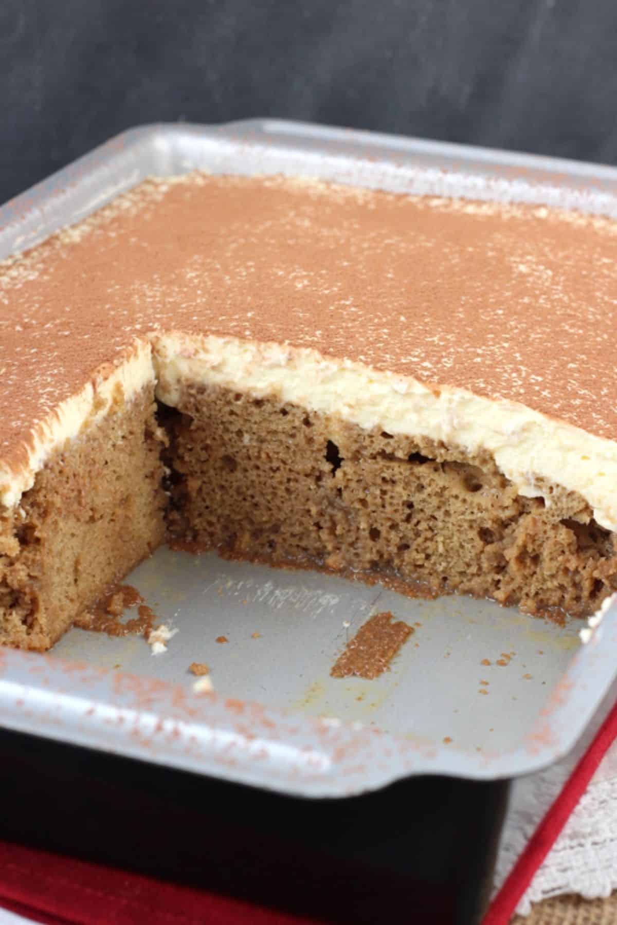 A tiramisu poke cake in a baking pan with several slices removed to show inside of cake.