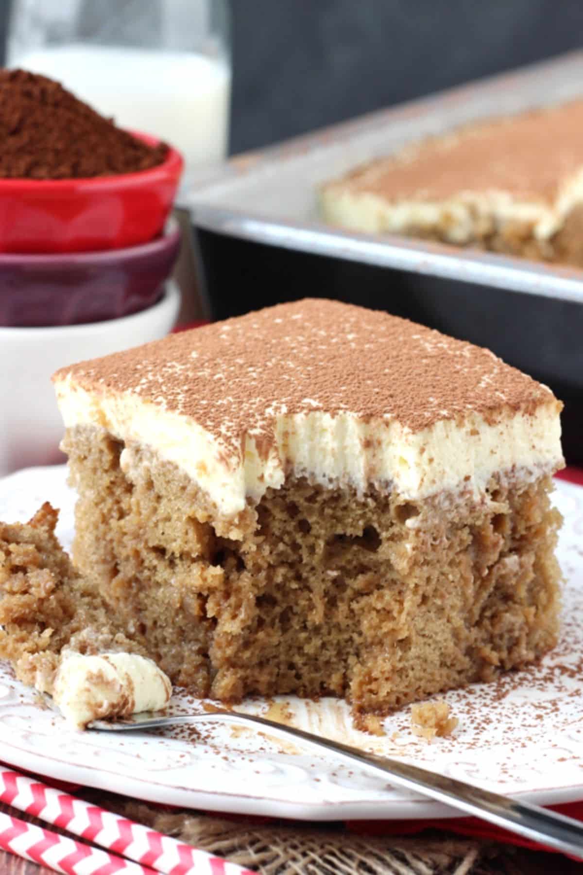 A slice of tiramisu poke cake on a white plate with a bite removed on a fork.