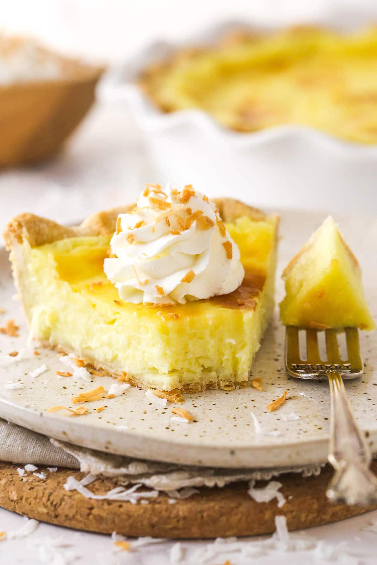 With a thick, creamy custard in a flaky, buttery pie crust, this coconut custard pie delivers just the right amount of coconut flavor. A slice of coconut custard pie on a white plate with a bite on the fork next to it.