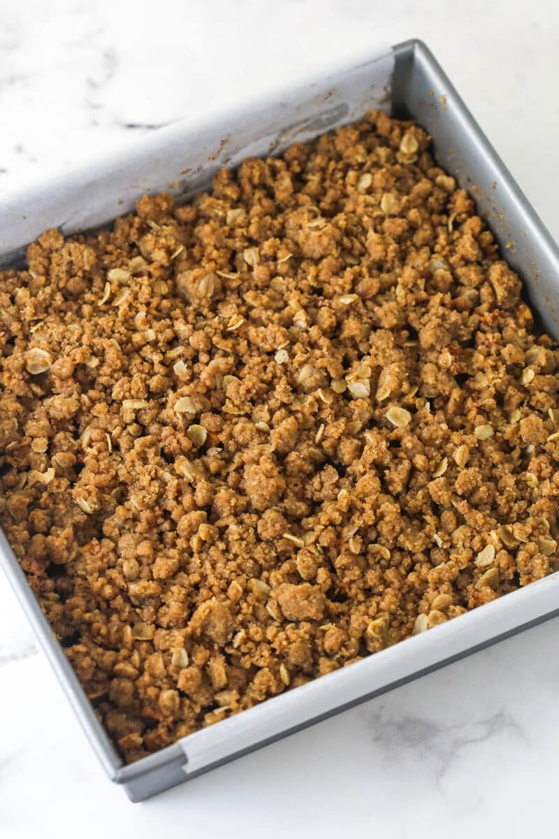 Apple pie bars offer all of the flavor of apple pie in a simple, easy-to-make bar, with shortbread crust, spiced apples, and crumble topping. Crumble topping on top of apple filling in a square pan