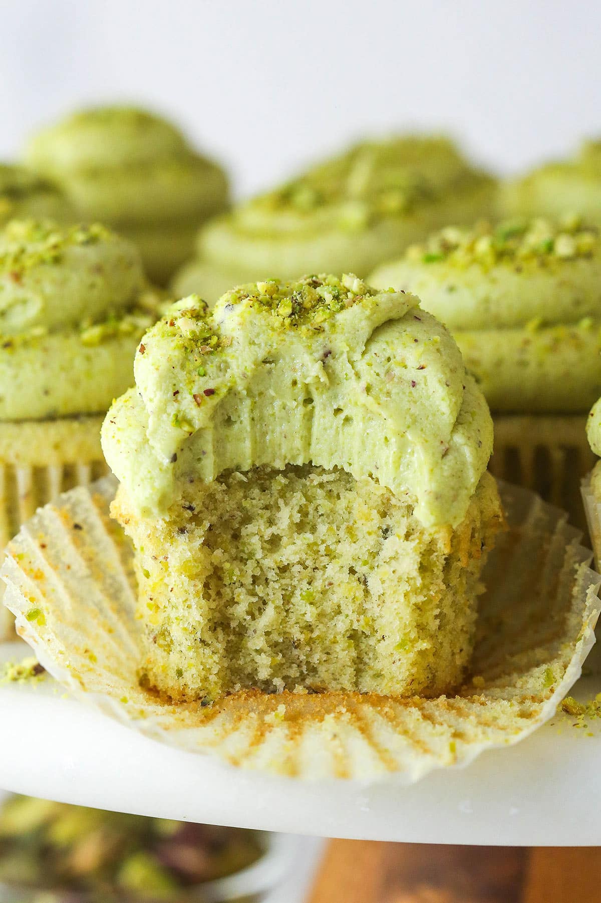 These pistachio cupcakes are full of real pistachios in the cupcakes and the buttercream, giving them their beautiful color and nutty flavor. A pistachio cupcake with the wrapper pulled down and a bite missing