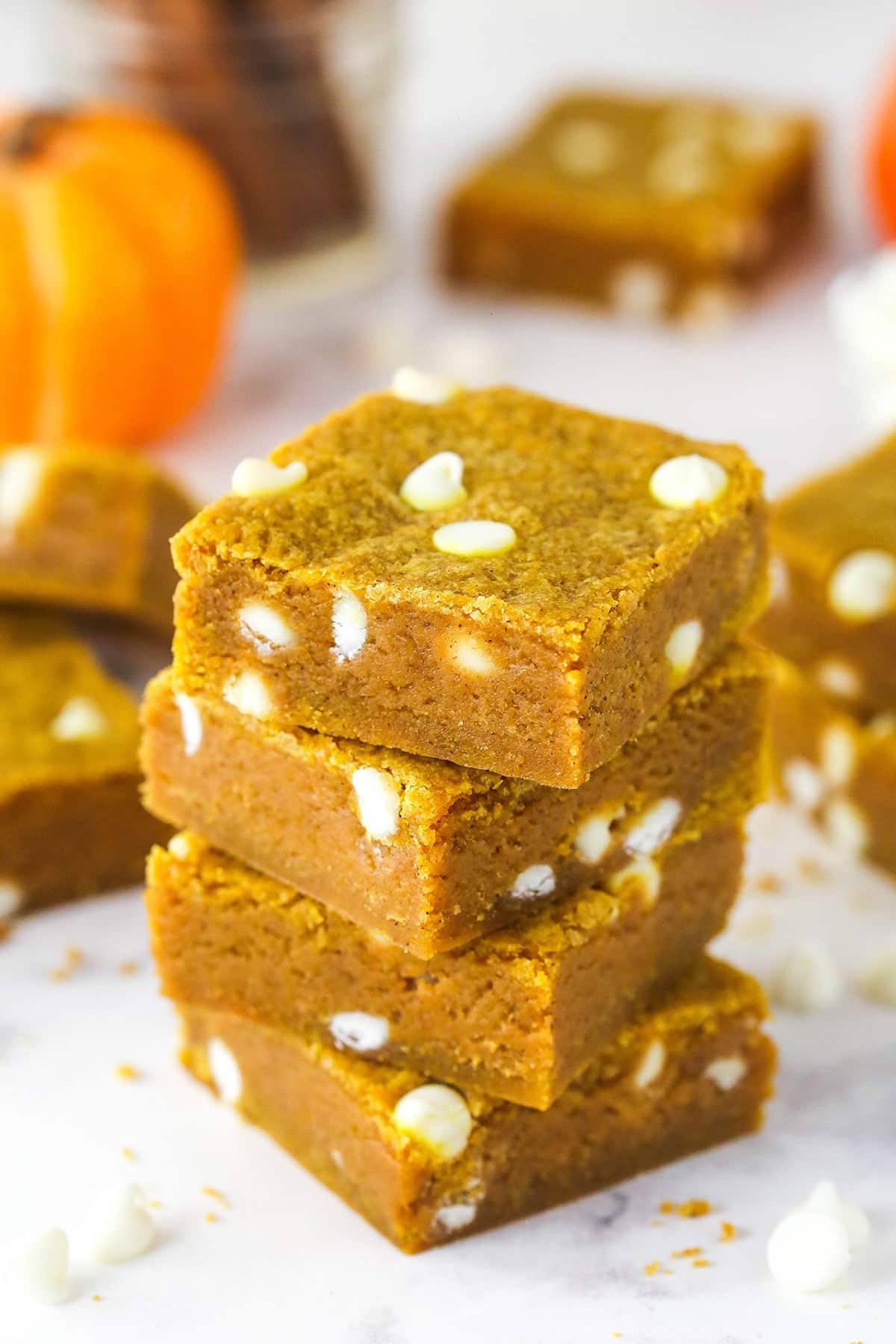 These pumpkin blondies are perfectly soft (but not cakey!) and chewy, dotted with white chocolate chips and full of fall flavors. Angled overhead view of a stack of 4 pumpkin blondies