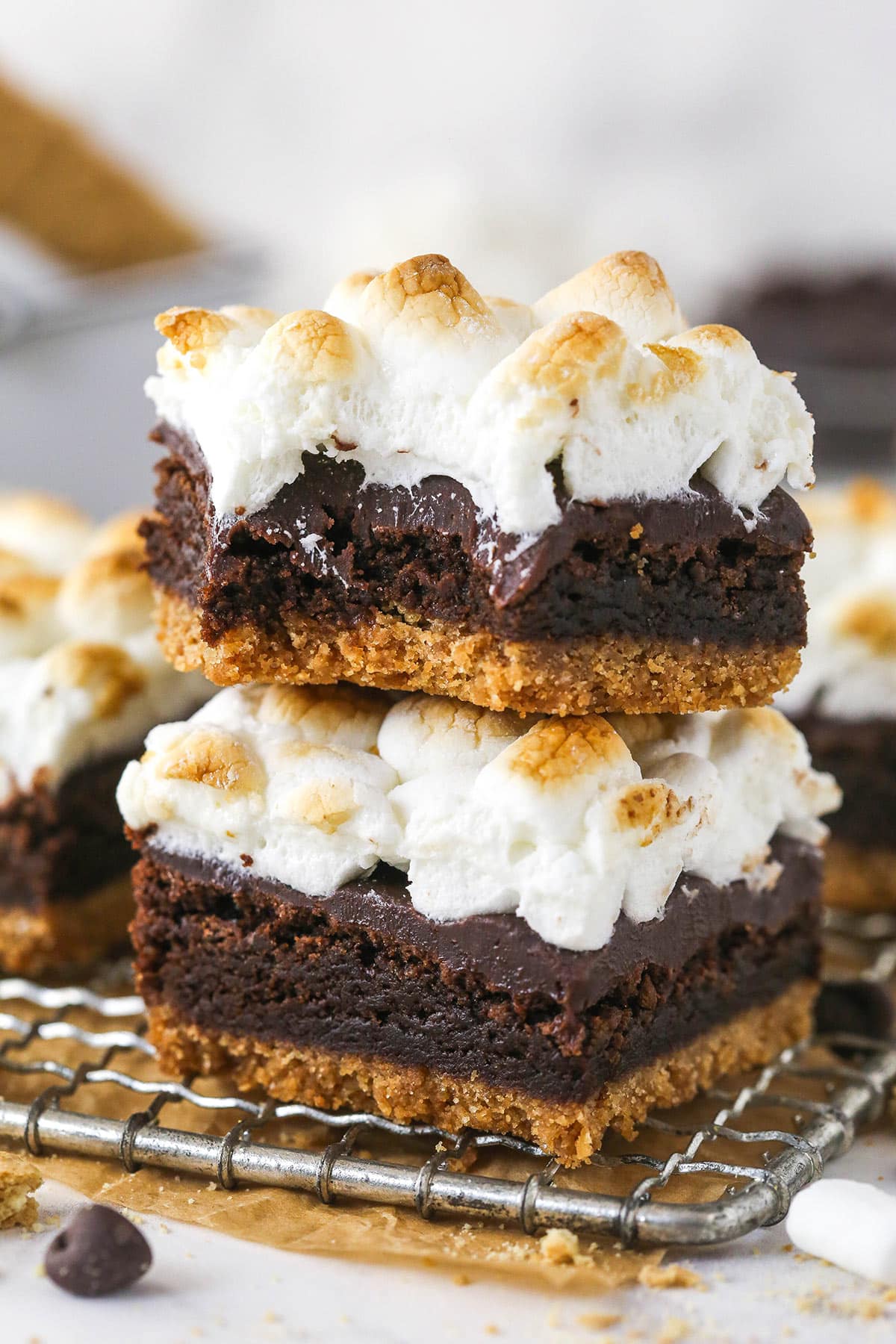 These s'mores brownies have all the classic flavors, with a graham cracker crust, fudgy brownies, ganache, and toasted marshmallows. Two s'mores brownies stacked on each other, the top one with a bite missing