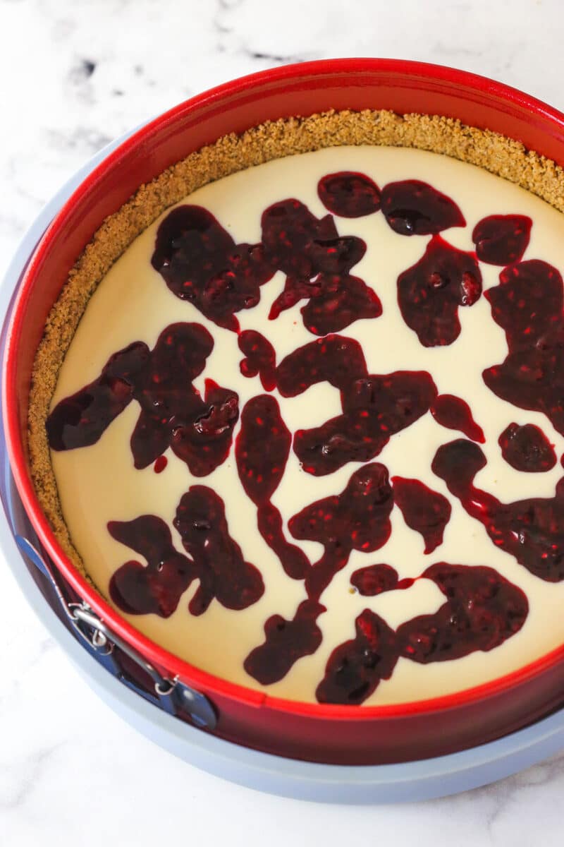 cheesecake batter in the springform pan with berry filling spooned over top