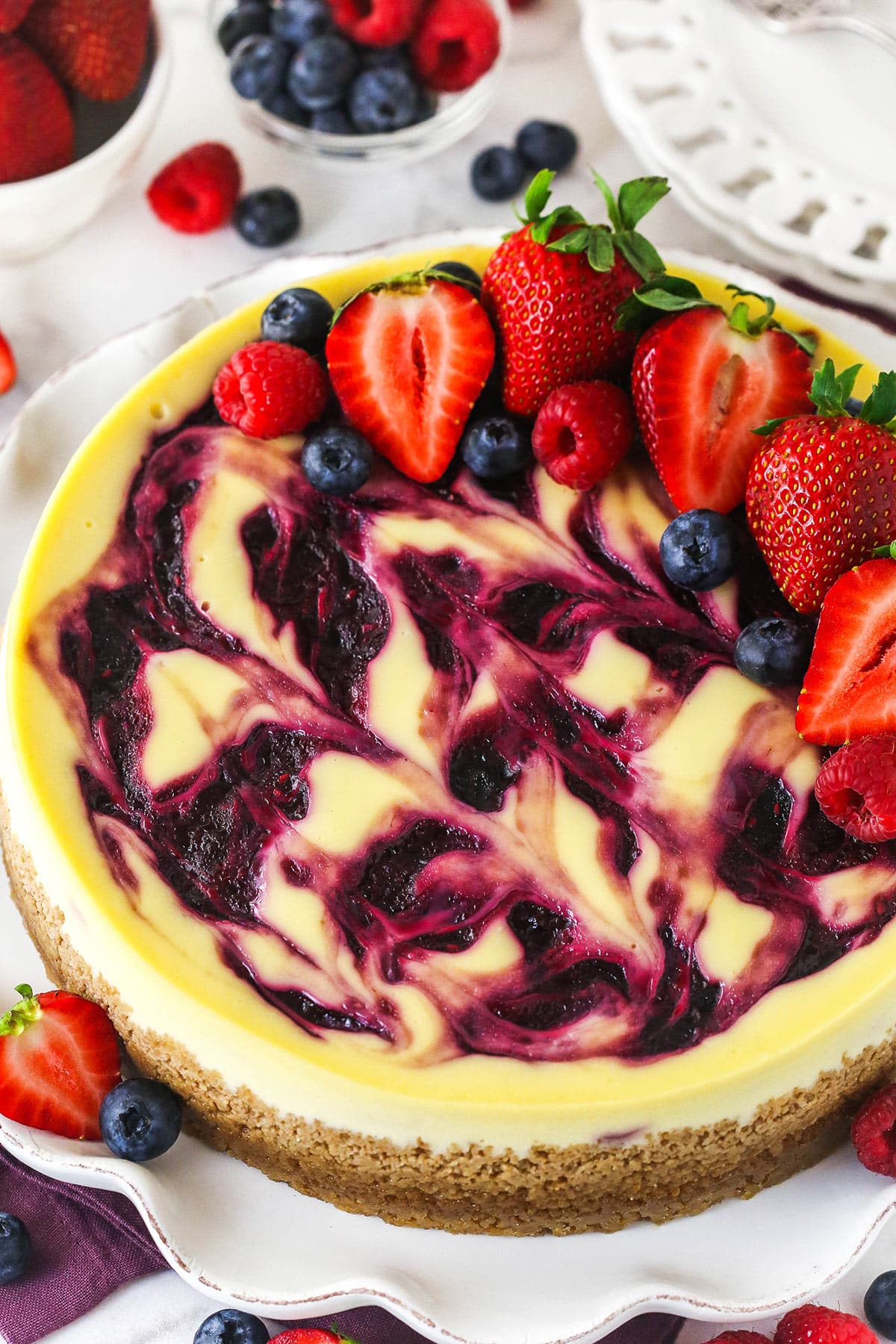 triple berry cheesecake on white ruffle platter with fruit around it