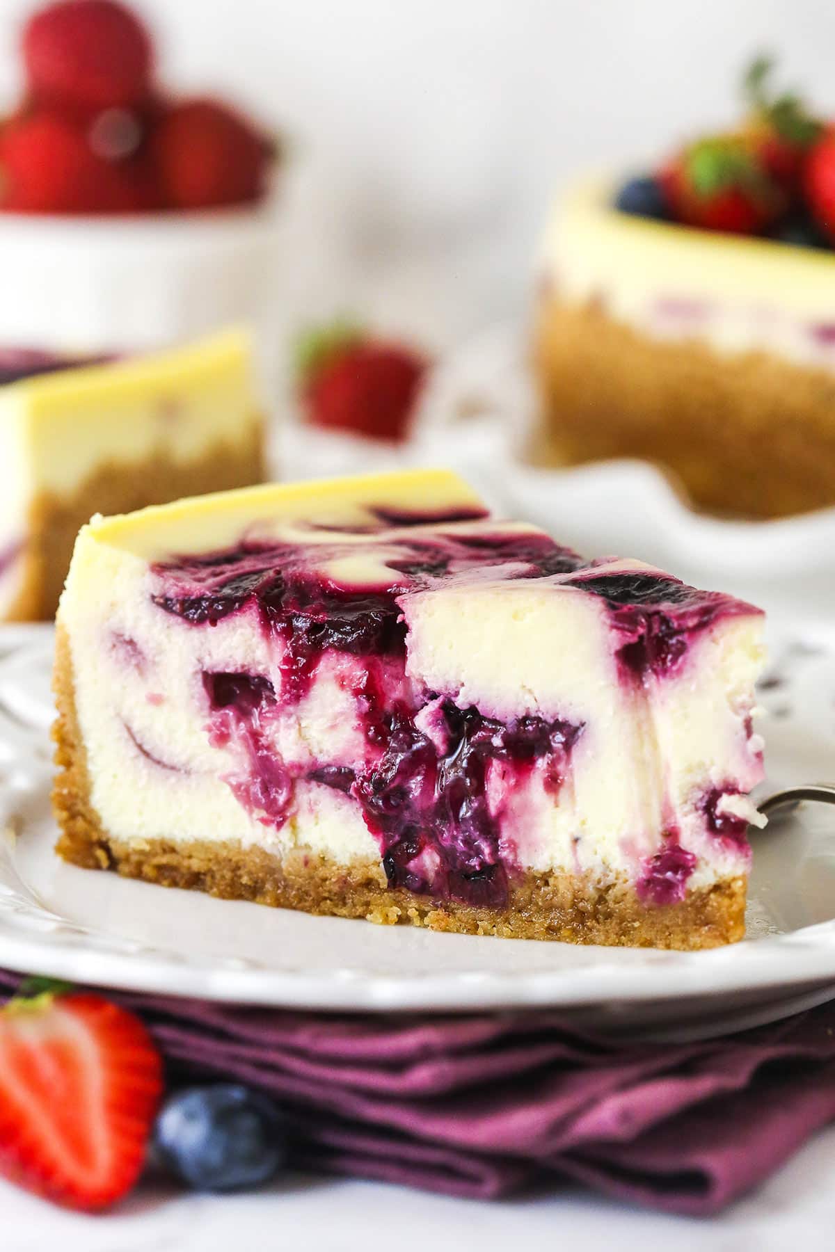 slice of triple berry cheesecake on white plate