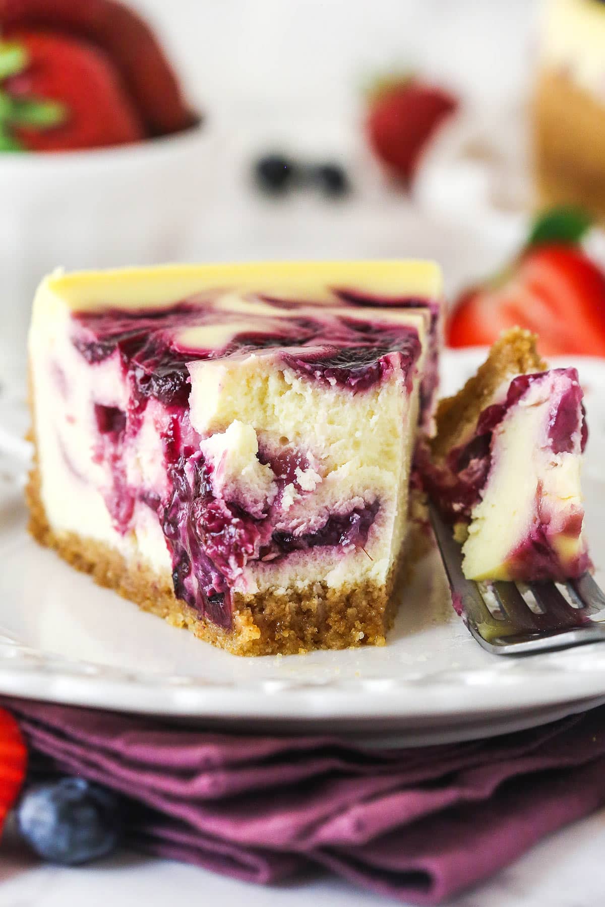 slice of triple berry cheesecake on white plate with a bite taken out