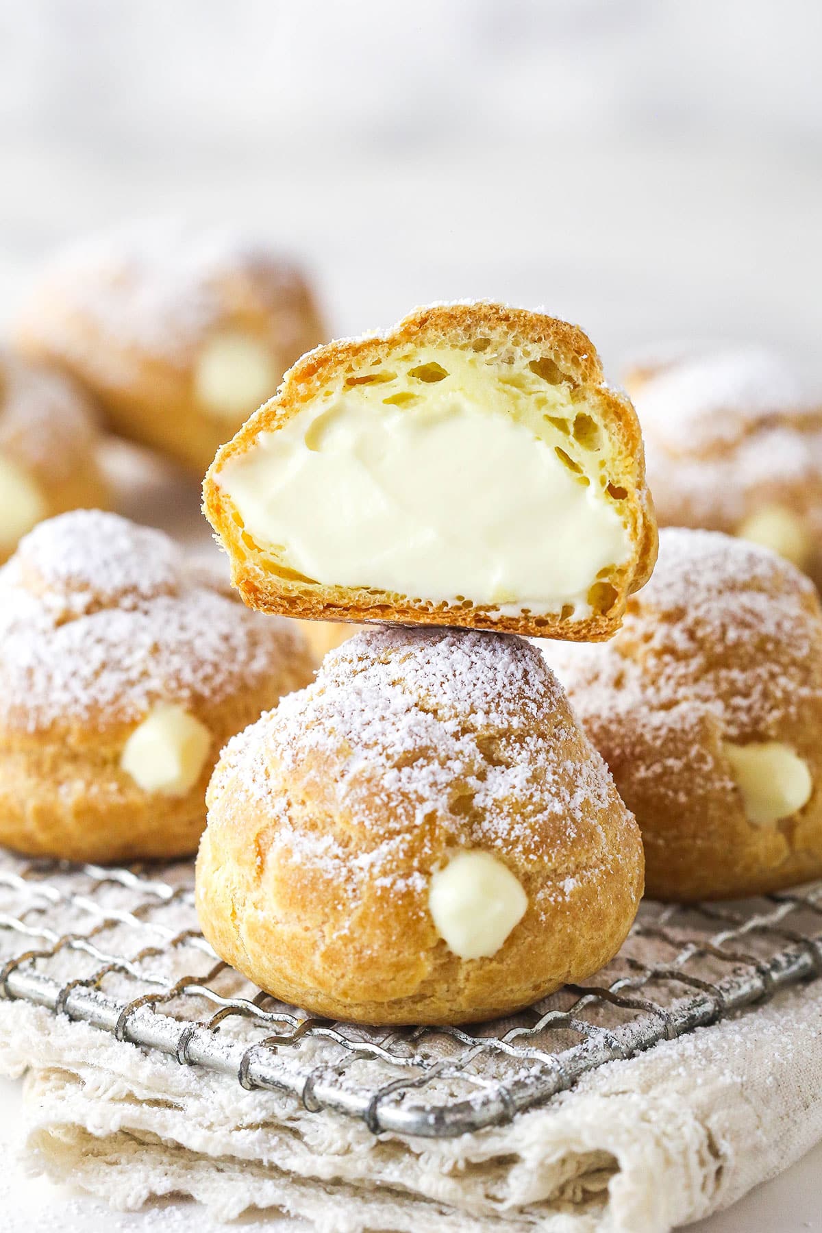 Master making cream puffs fit for a bakery and perfect for sharing with my in-depth tips and step-by-step photos. Cream puffs on a cooling rack, one cut in half to show the inside