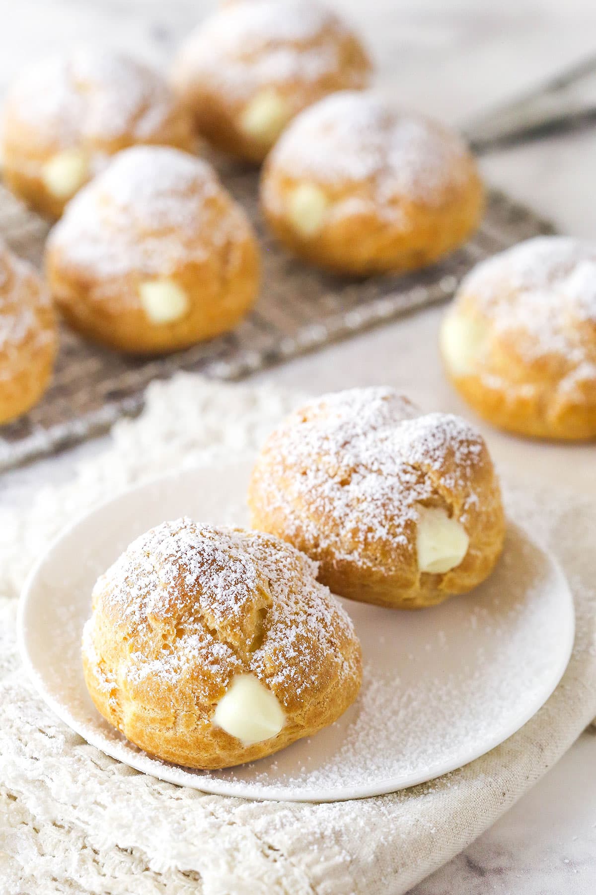 Master making cream puffs fit for a bakery and perfect for sharing with my in-depth tips and step-by-step photos. Tw0 cream puffs on a white plate