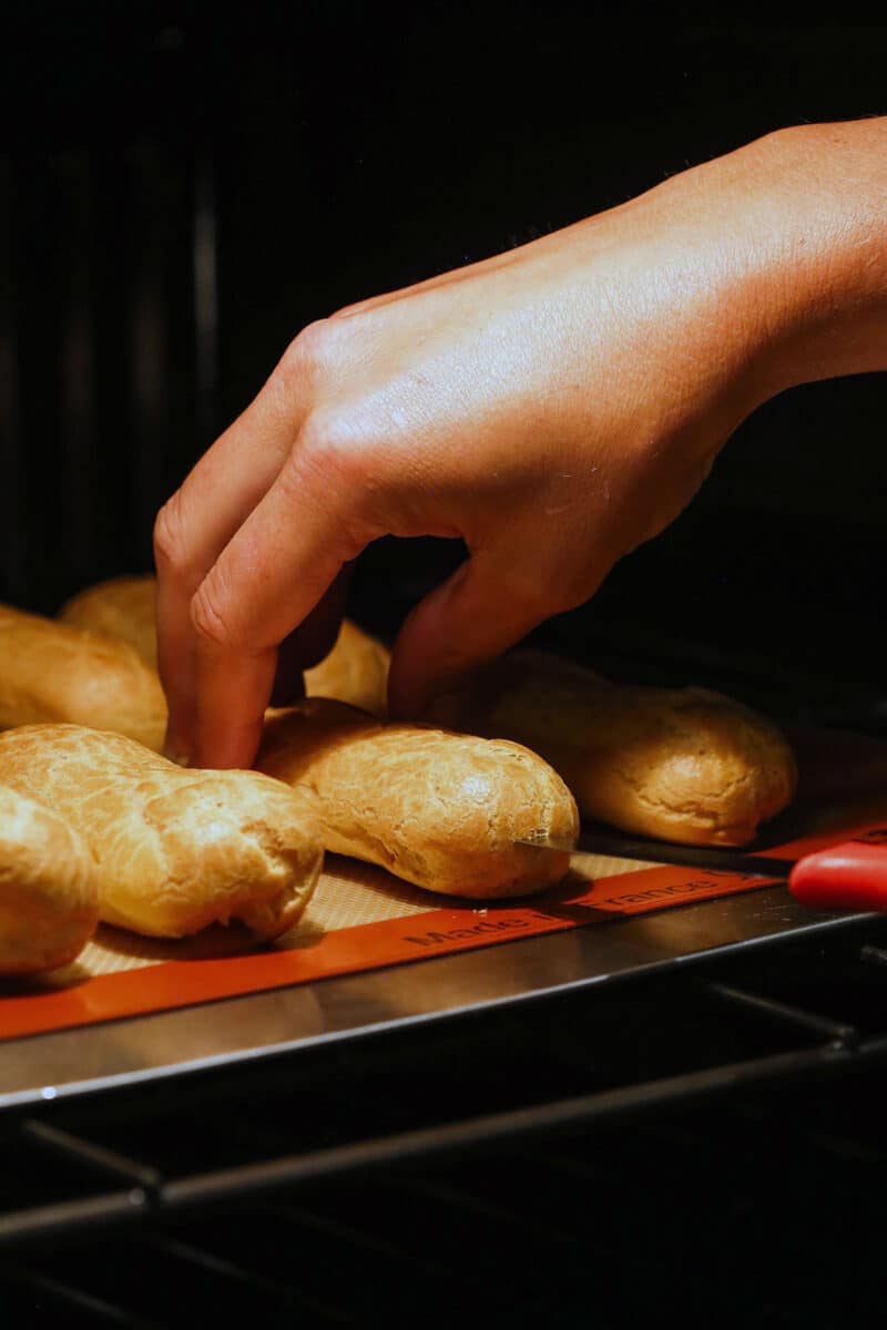 A hand touching pastry shells in the oven