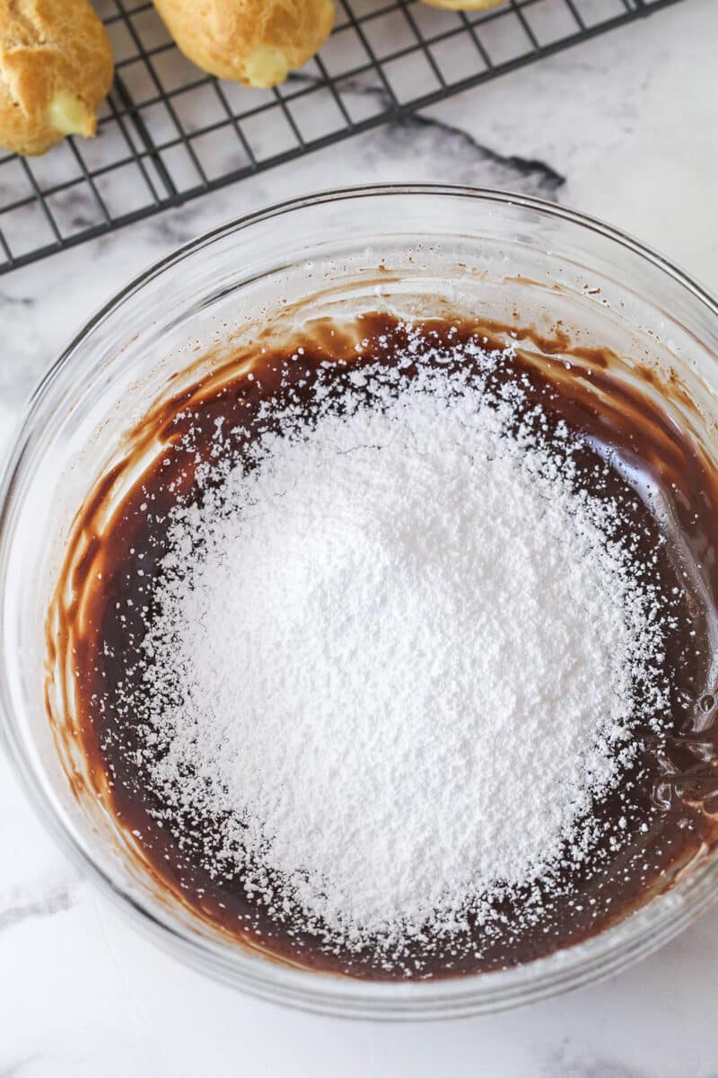 Mastering eclairs at home is easier than you think with my step-by-step photos and in-depth tips. Made with pastry cream & chocolate glaze. Stirring powdered sugar into melted chocolate