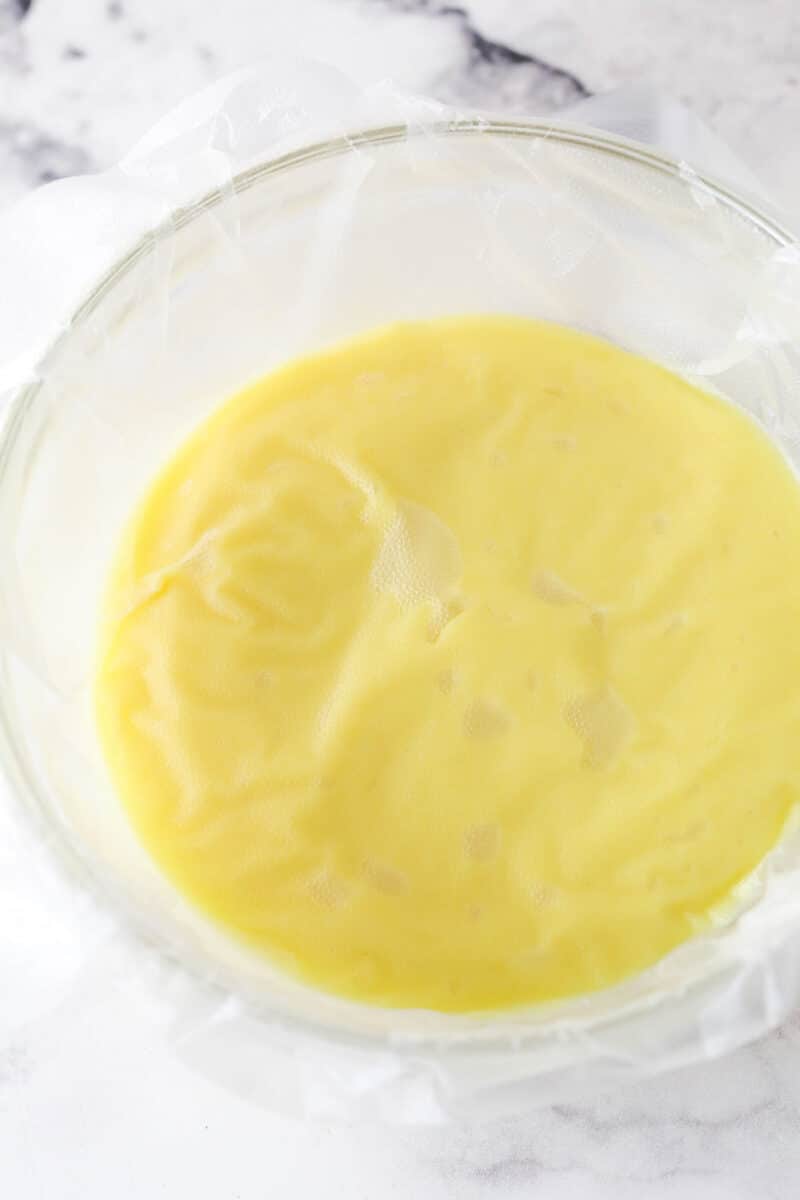 Mastering eclairs at home is easier than you think with my step-by-step photos and in-depth tips. Made with pastry cream & chocolate glaze. Pastry cream covered with clear wrap in a bowl