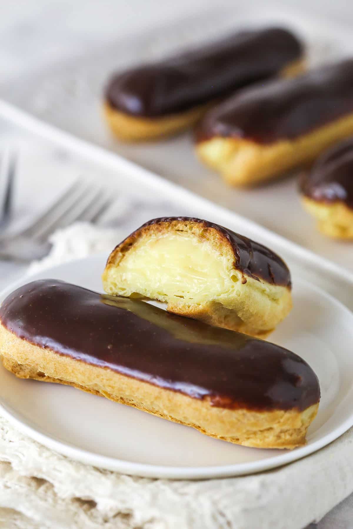 Mastering eclairs at home is easier than you think with my step-by-step photos and in-depth tips. Made with pastry cream & chocolate glaze. Half of an eclair leaning against another one to show the inside