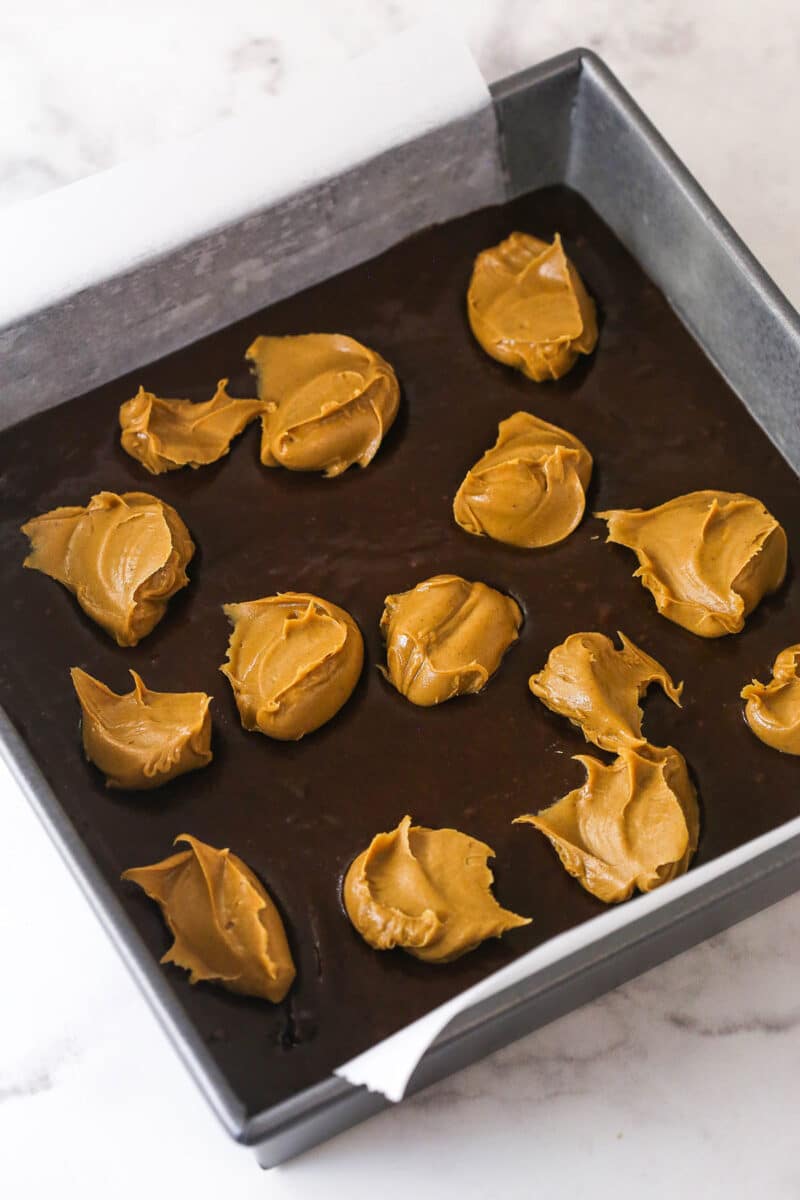 Creamy peanut butter is swirled into rich, chewy chocolate brownies in this easy Peanut Butter Brownies recipe. Dollops of peanut butter on brownie batter in a square pan