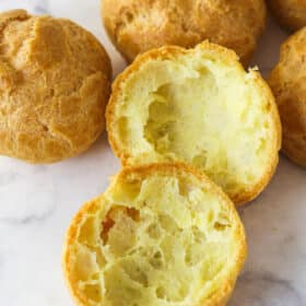 Choux pastry shells on the counter, one cut in half to show the hollow inside.