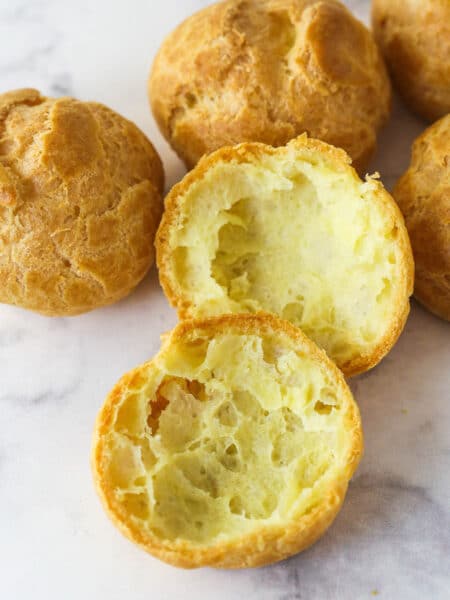 Choux pastry shells on the counter, one cut in half to show the hollow inside.