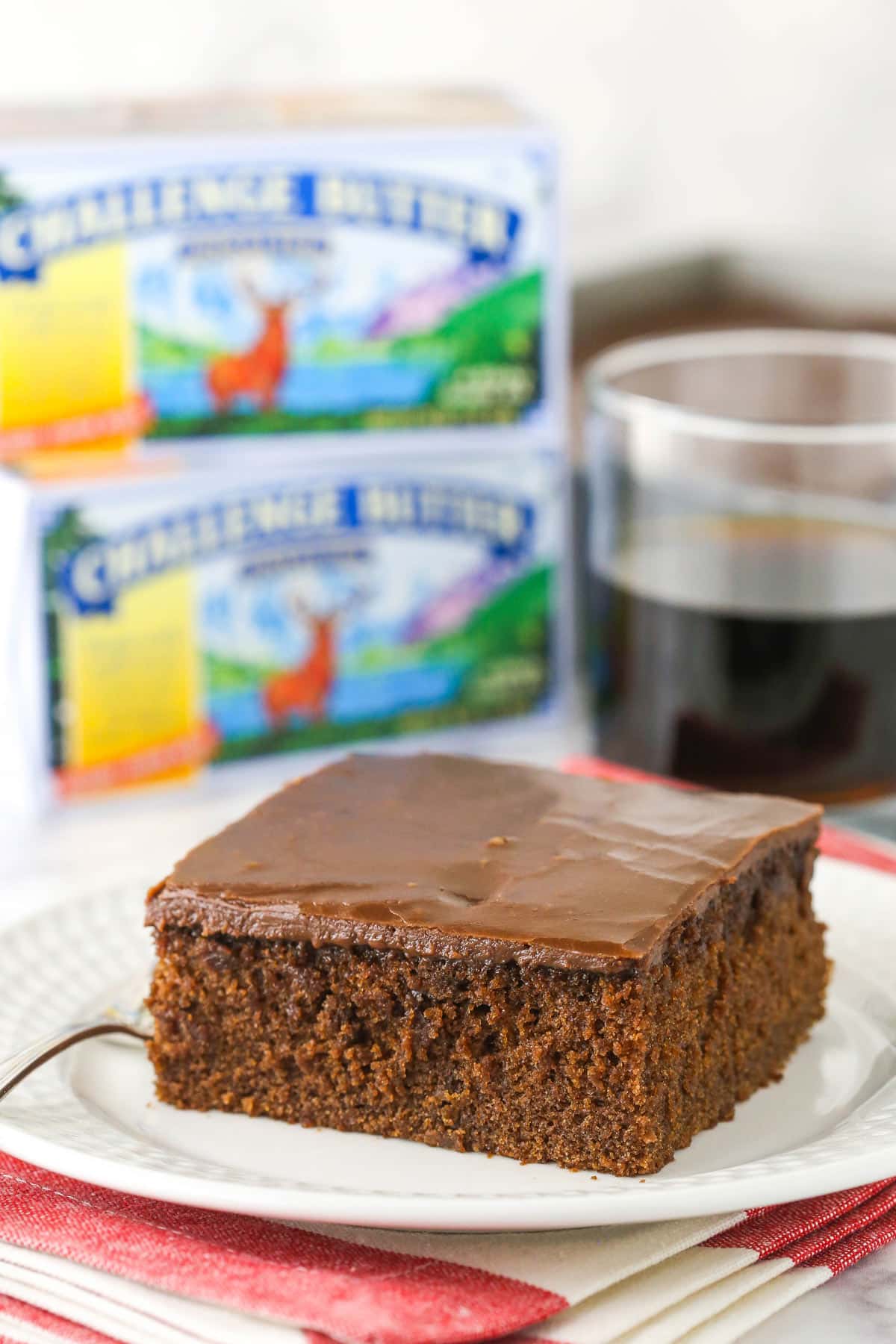 A slice of Coca Cola cake with on a white plate with boxes of butter in the background.