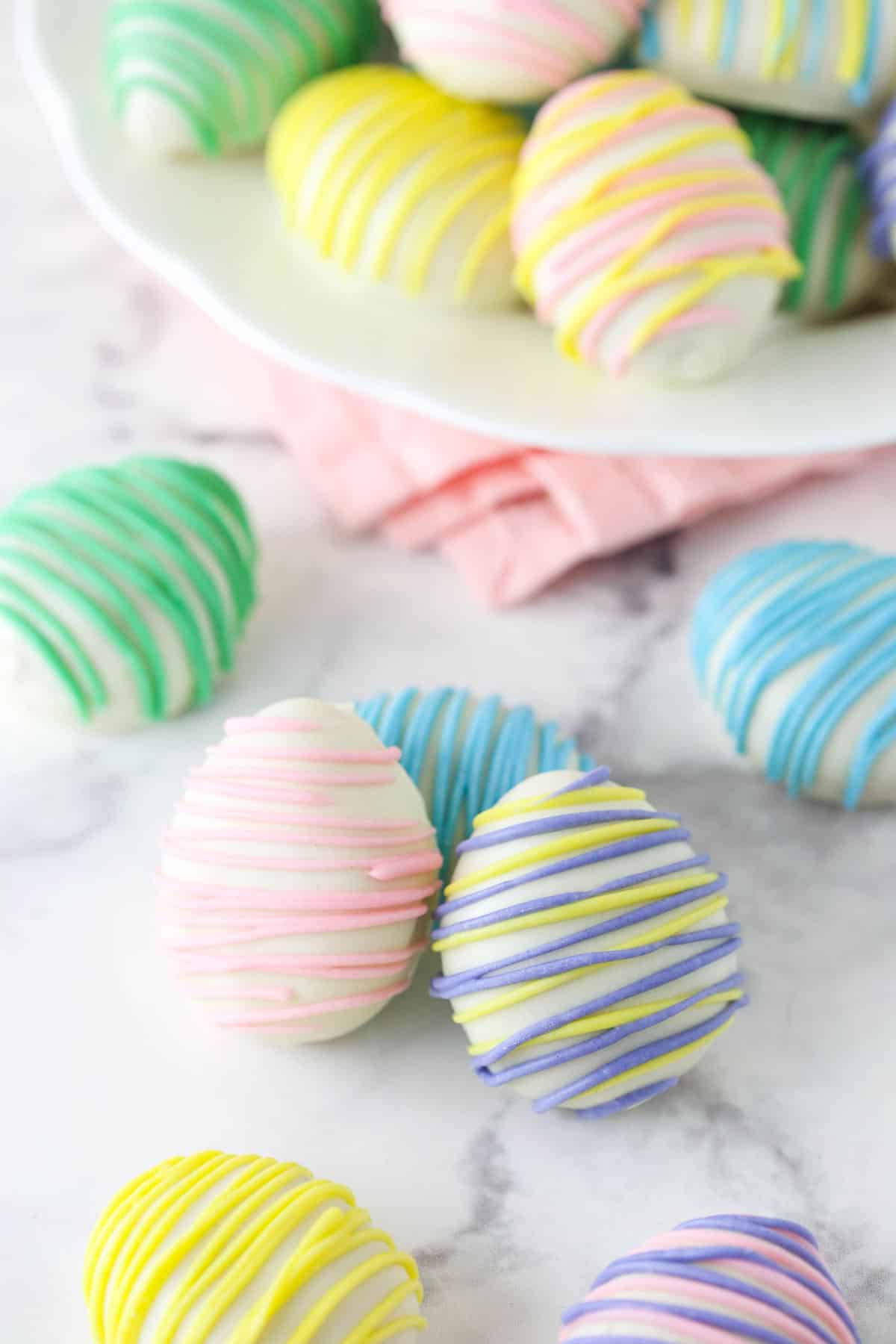 Several Easter egg Oreo cookie balls on a marble counter top with more on a white plate.