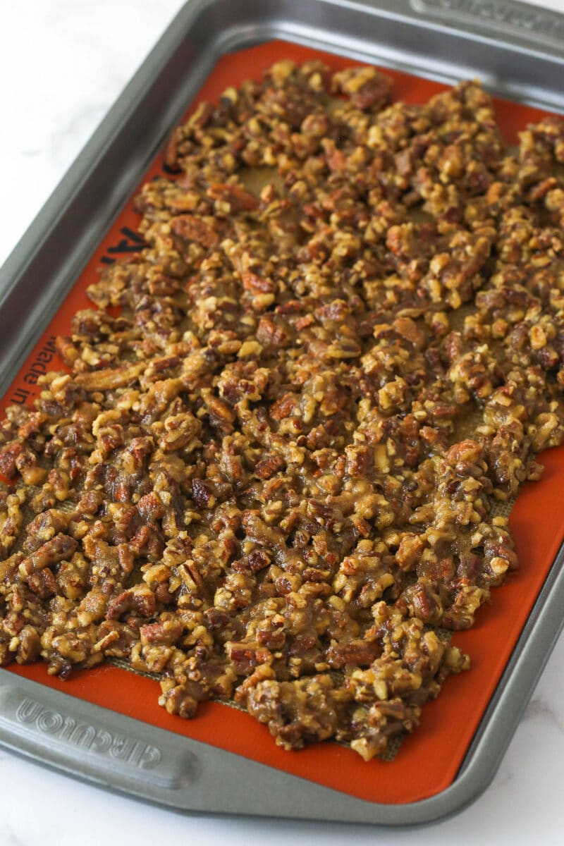 With layers of pumpkin cake, pecan praline crunch, and a caramel buttercream, this pecan praline pumpkin cake is impressive and delicious. Pecan praline spread on a baking sheet
