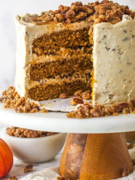 A pecan praline pumpkin cake on a cake stand with a slice missing