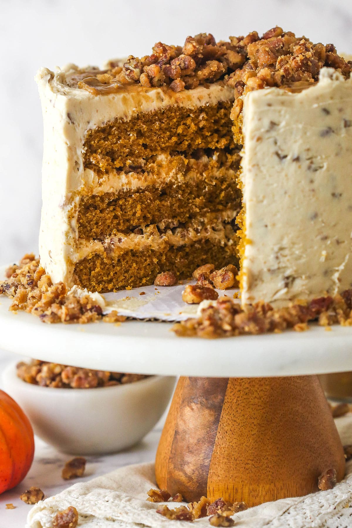 With layers of pumpkin cake, pecan praline crunch, and a caramel buttercream, this pecan praline pumpkin cake is impressive and delicious. A pecan praline pumpkin cake on a cake stand with a slice missing