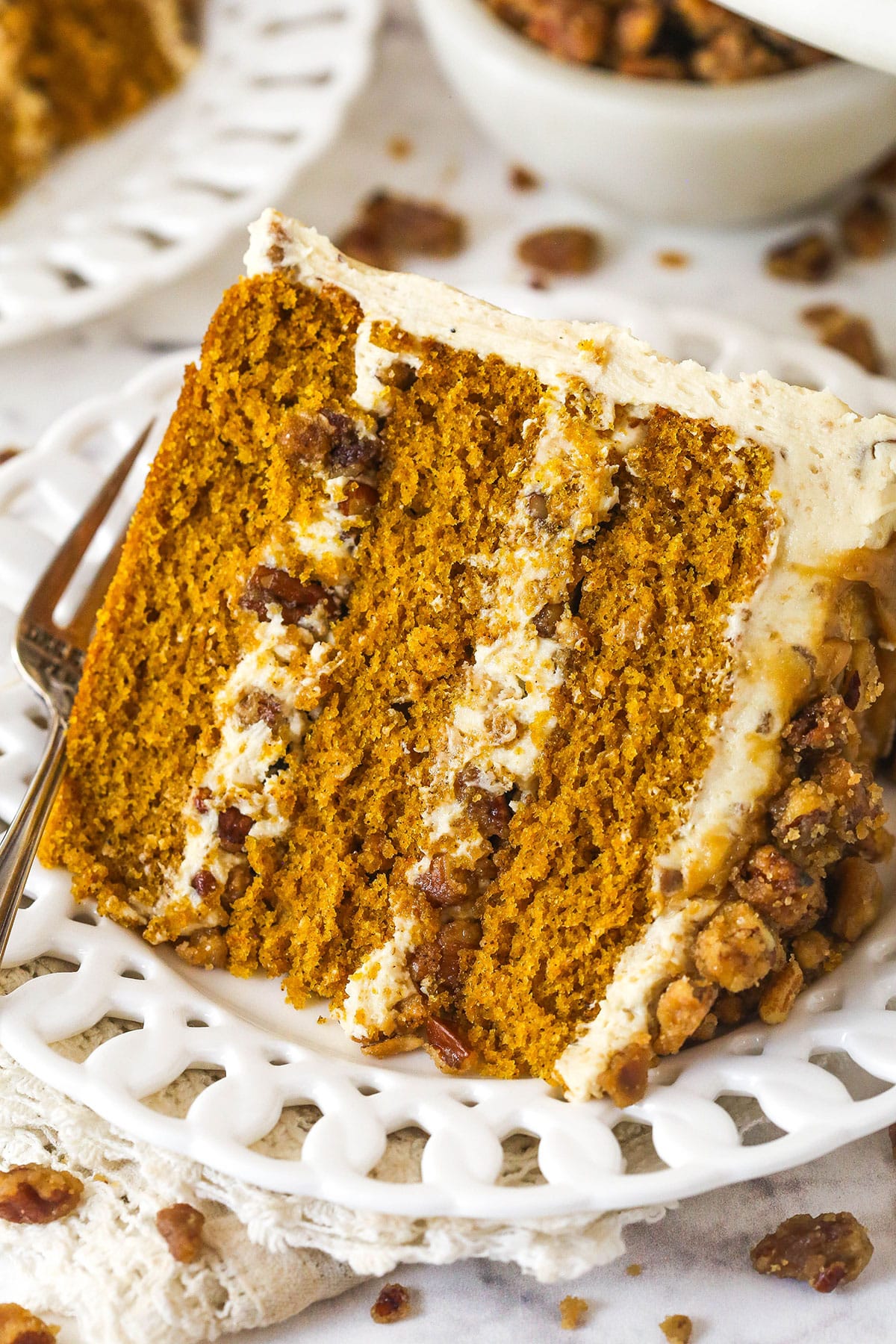 With layers of pumpkin cake, pecan praline crunch, and a caramel buttercream, this pecan praline pumpkin cake is impressive and delicious. Close up of a slice of pecan praline pumpkin cake on a white palte