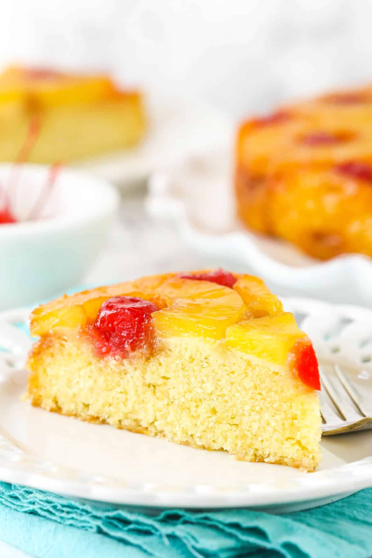 Soft and buttery with caramelized pineapple and cherries, this Pineapple Upside Down Cake has the perfect texture and lots of flavor! A slice of pineapple upside down cake on a small white plate.