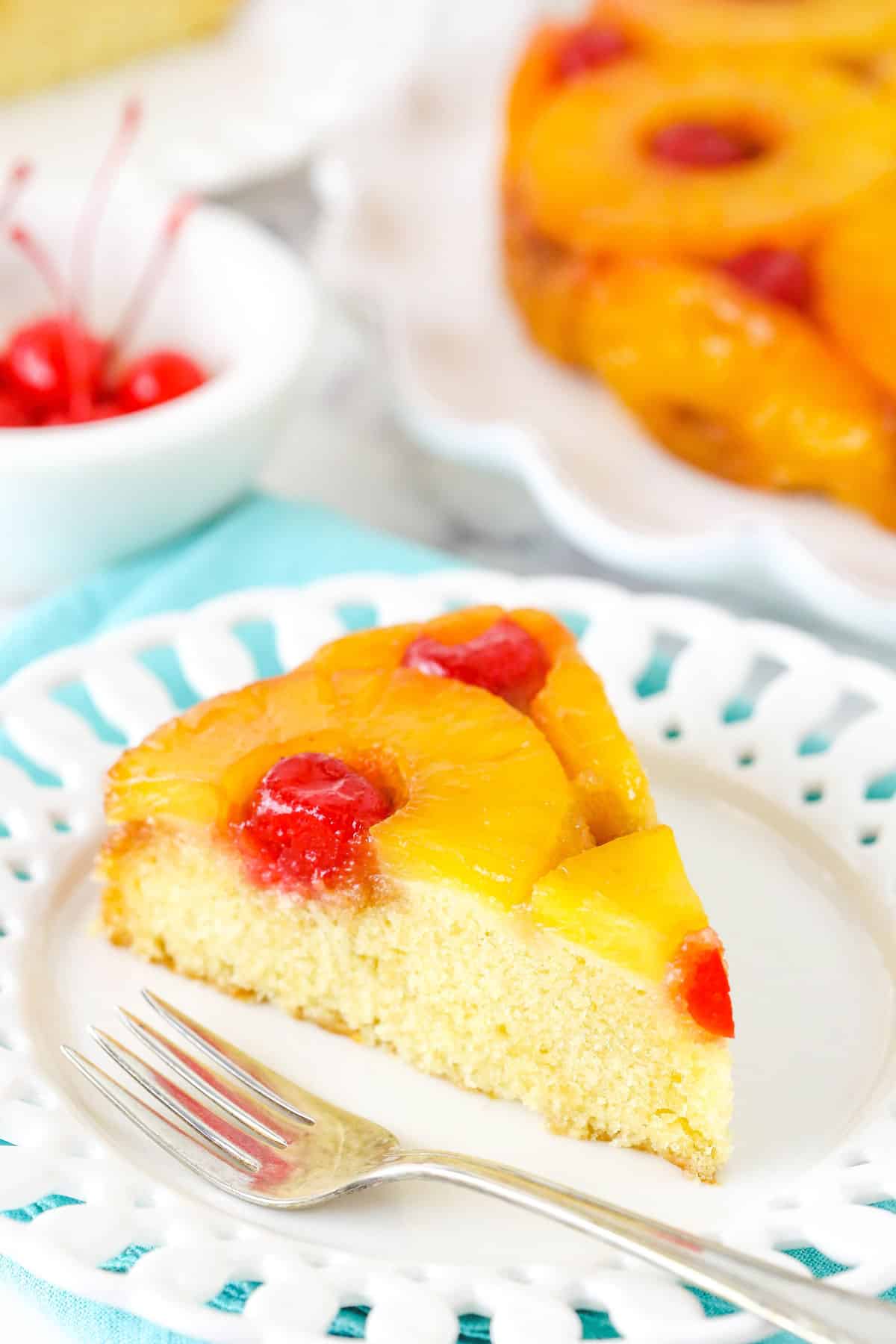 Soft and buttery with caramelized pineapple and cherries, this Pineapple Upside Down Cake has the perfect texture and lots of flavor! A slice of pineapple upside down cake on a small white plate.