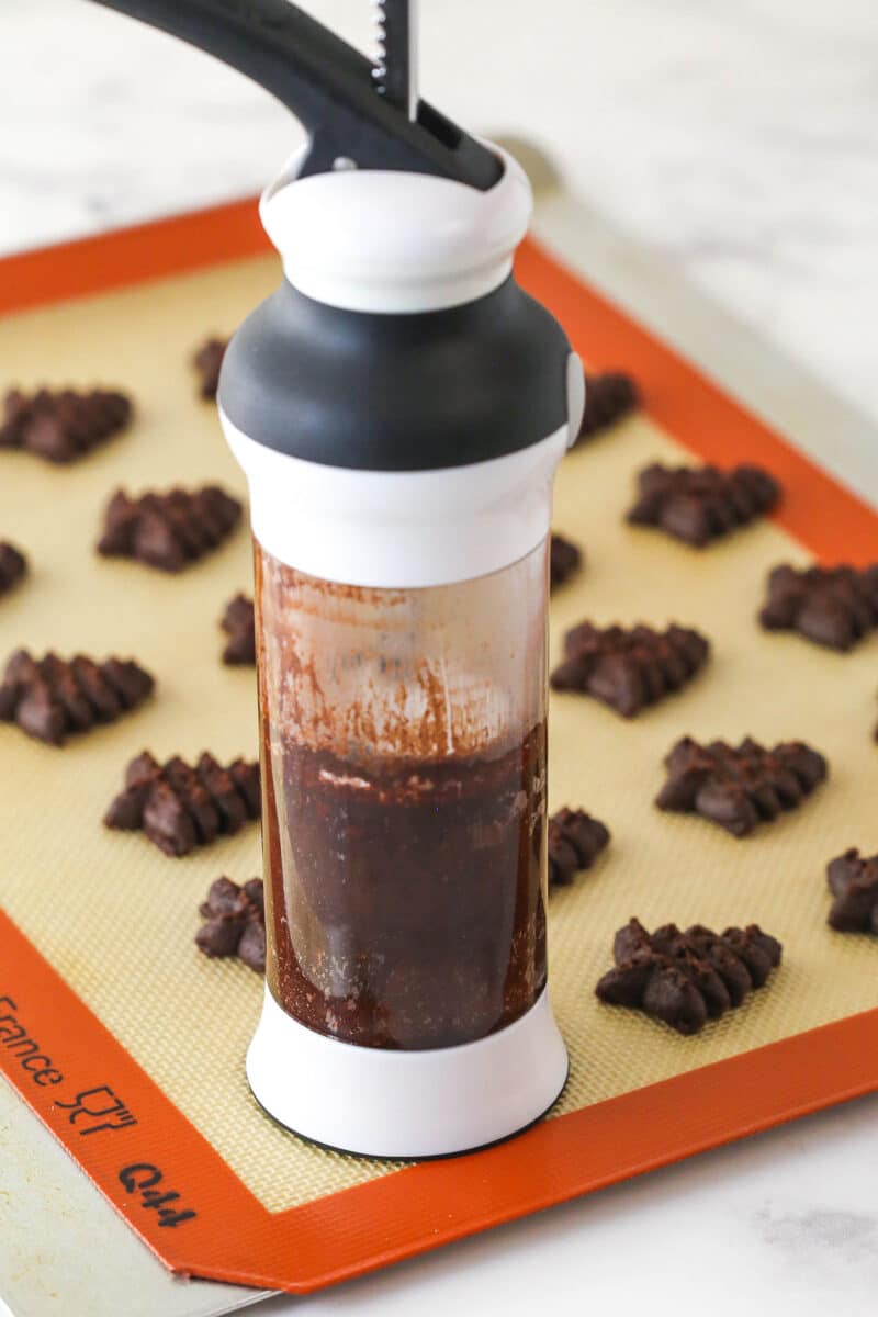 cookie press adding chocolate spritz cookies onto baking mat