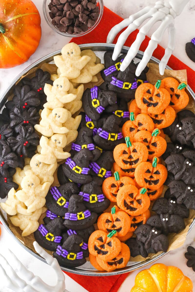overhead image of Halloween chocolate spritz cookies on grey tray with skeleton hands around it