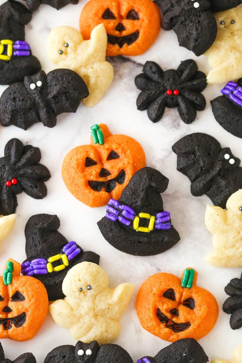 Halloween spritz cookies laid out on white marble background with a focus on a witch hat and jack-o-lantern