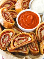 Closeup of pepperoni rolls with marinara sauce and parmesan cheese on a serving tray lined with parchment paper.