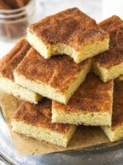 Snickerdoodle cookie bars stacked on a plate. The top bar has a bite taken out of it.