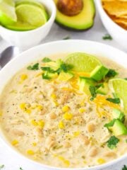 Close up of a bowl of Instant Pot white chicken chili garnished with fresh lime wedges and diced avocado.
