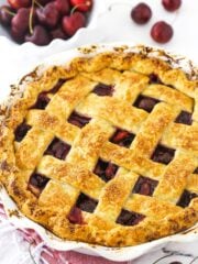 A cherry pie inside of a 9-inch pie dish with a bowl of sweet cherries in the background