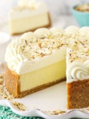 An almond mousse cheesecake on a serving platter with one slice removed and featured in the background